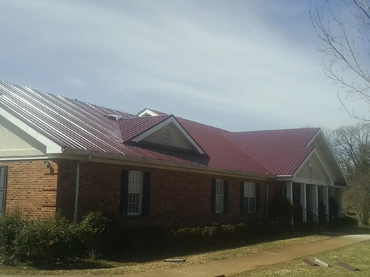 Red metal roof with gabled entries on a long brick building, from a Hail Damage Roof Repair job in Fort Atkinson