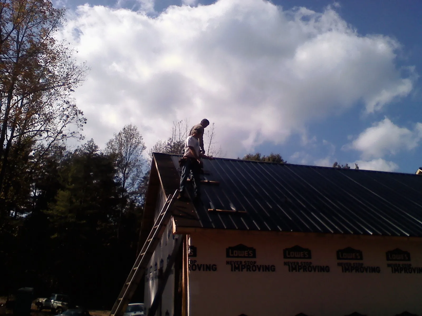 Roofer fastening dark metal panels high against a cloudy sky, from a Roof Inspection job in Fort Atkinson