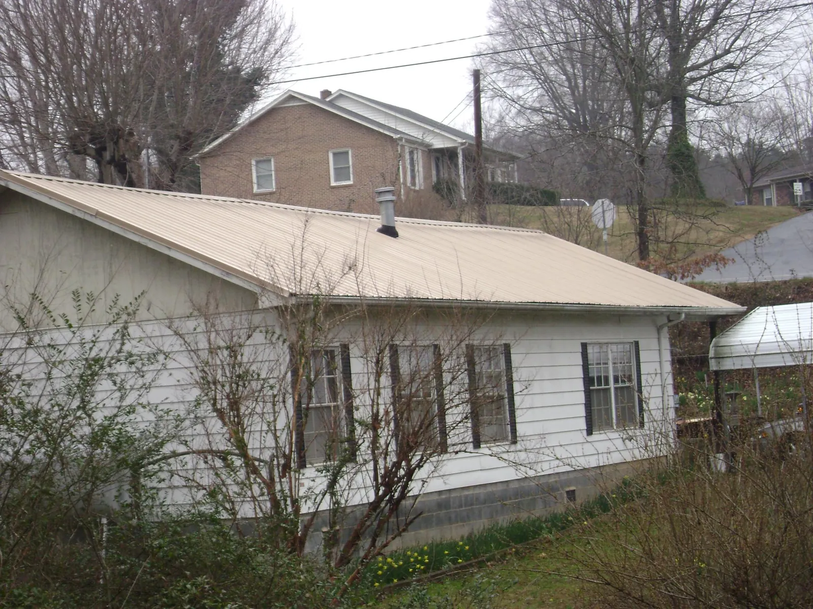 Tan metal roof on a white sided house set into a hillside — Commercial Roofing by Roofing Brothers in Fort Atkinson